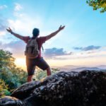 travel  Young trekking man standing on rocky mountain peak